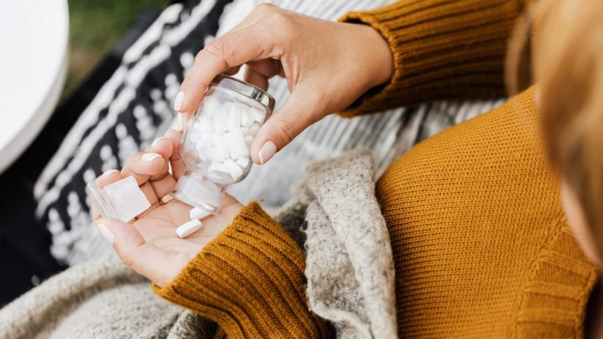 Close-up of a person holding a glass bottle with white pills, captured indoors.